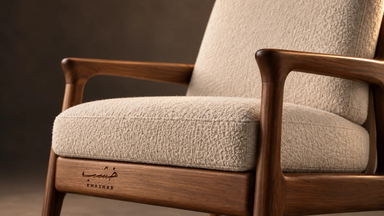 Close-up of a modern walnut armchair with cream bouclé upholstery, warm lighting and an engraved Khashab logo